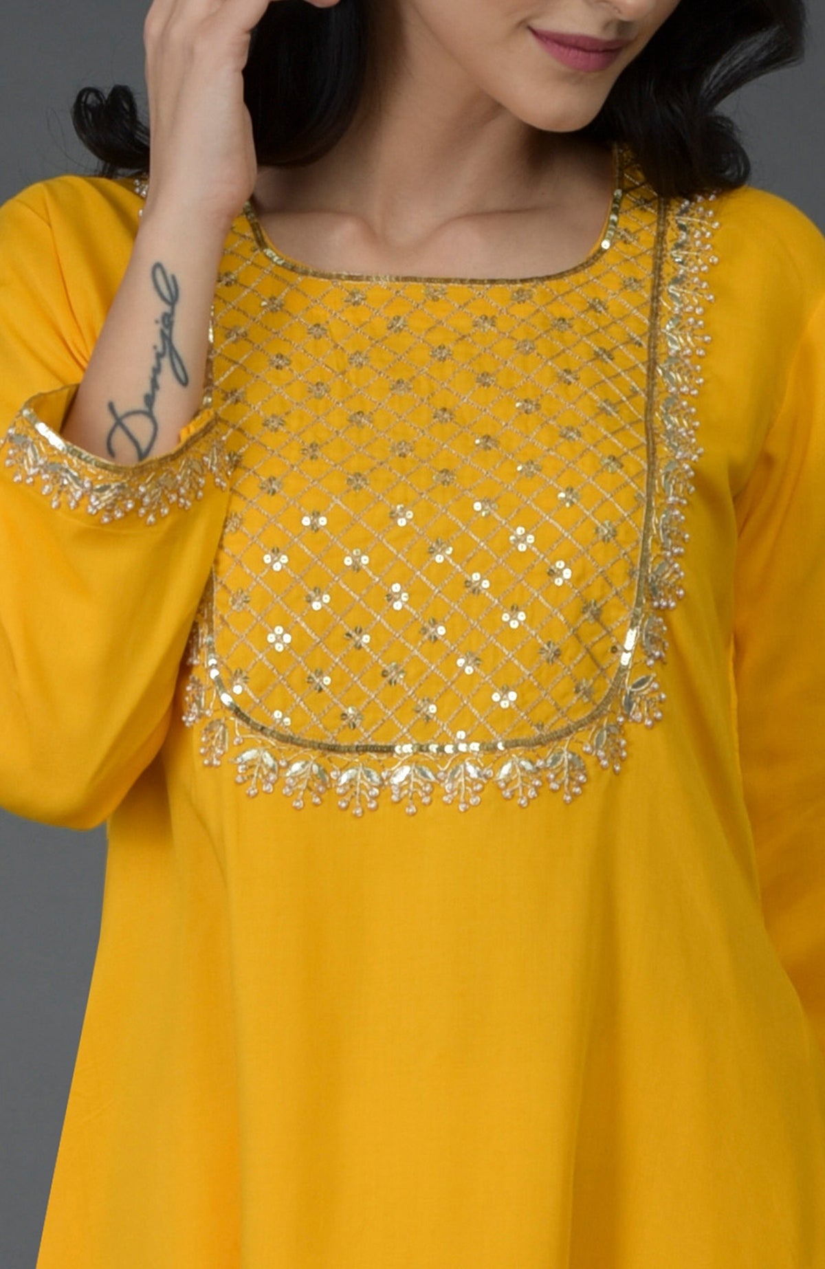 A woman models a yellow kurta with intricate gold and silver embroidery.