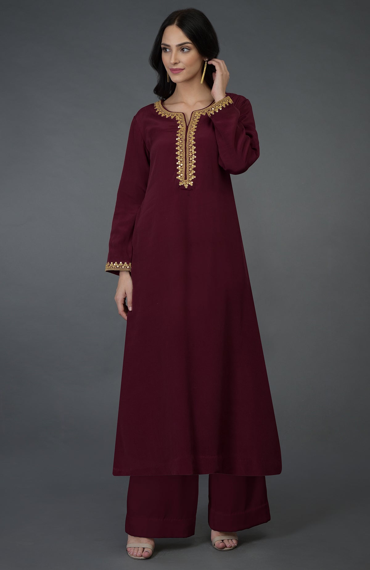 A woman models a burgundy kurta set with gold embroidery and sequins.