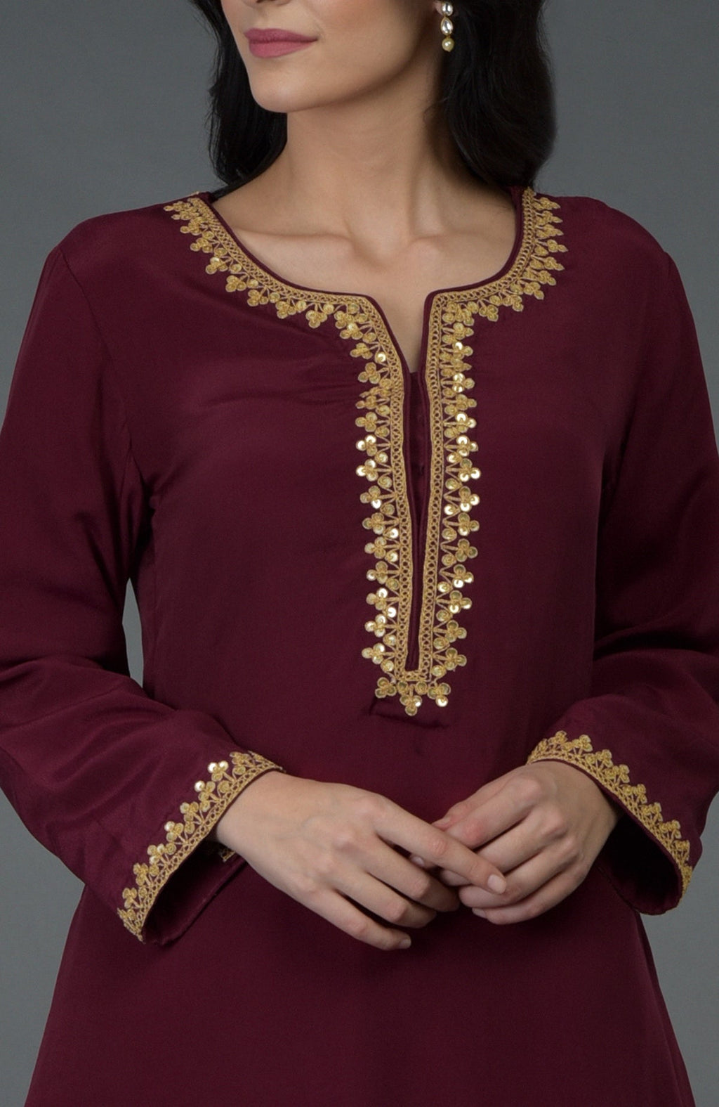 A woman models a burgundy tunic with gold marori and sequin embroidery.