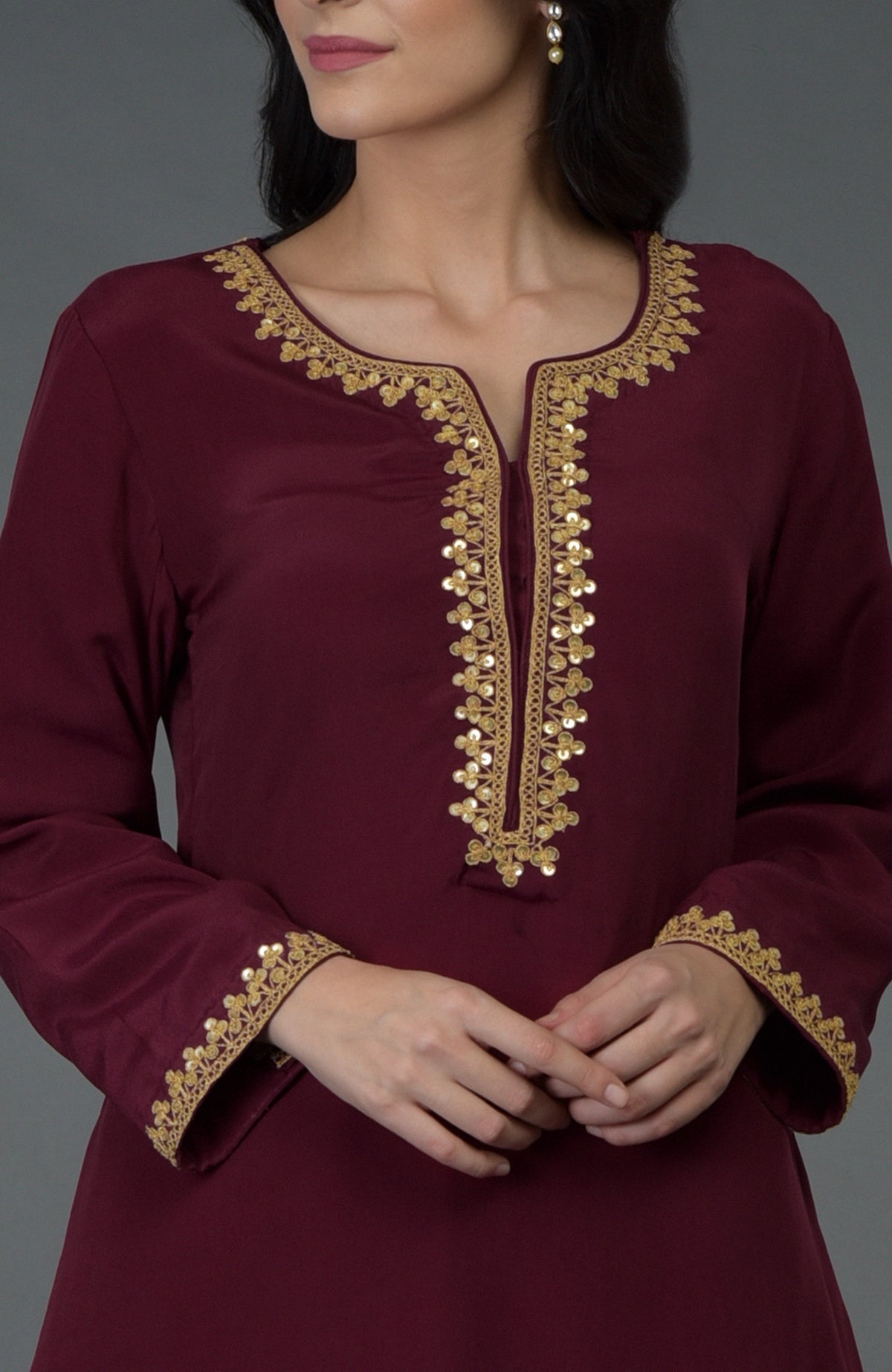 A woman models a burgundy tunic with gold marori and sequin embroidery.