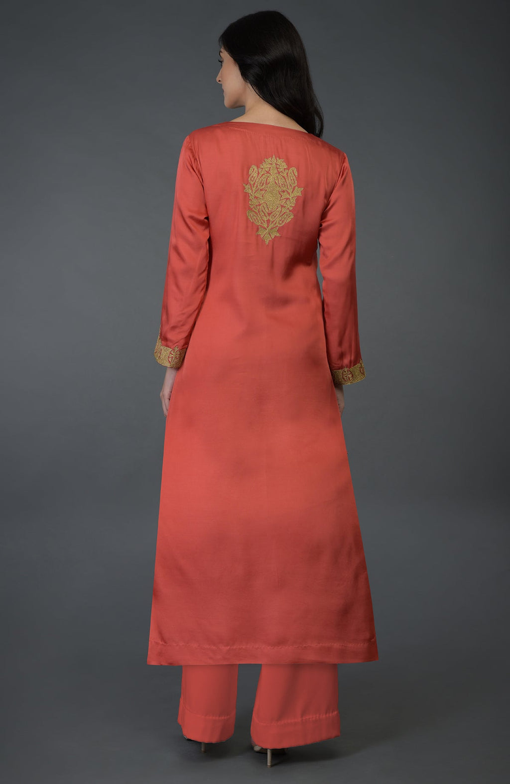 A woman models a living coral Kashmiri tilla embroidered kurta set from the back.