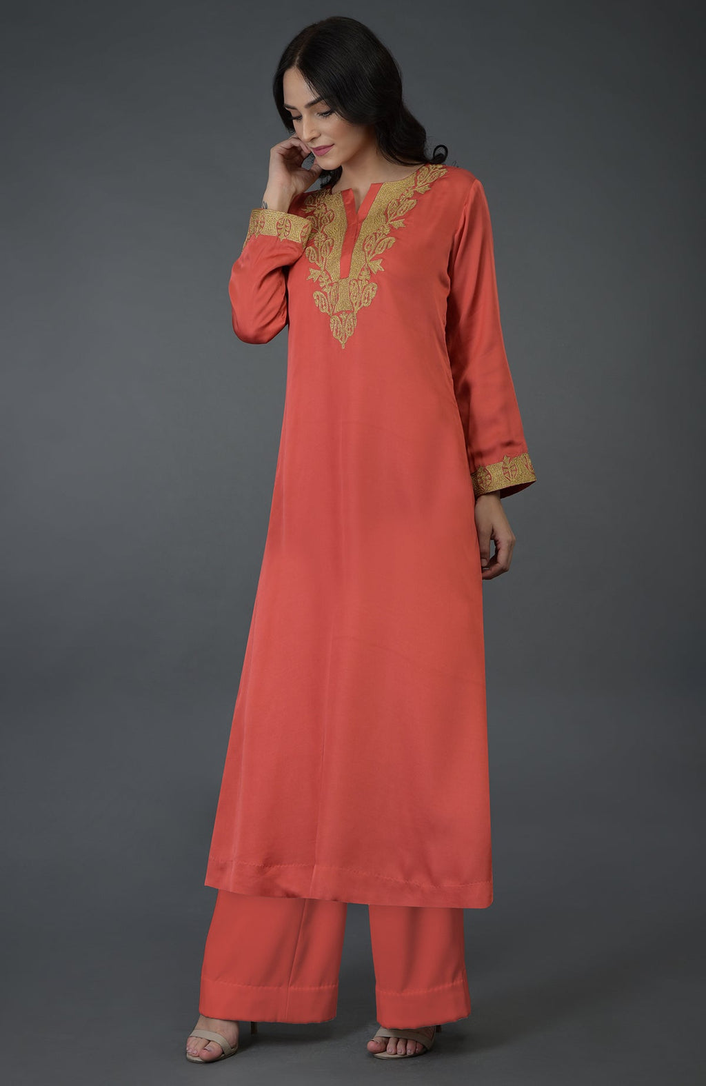 A woman models a living coral Kashmiri tilla embroidered kurta set with gold embroidery.