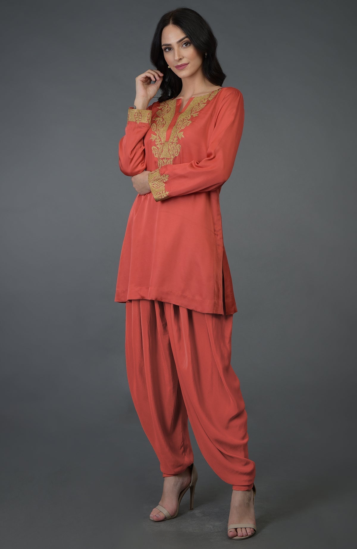 A woman models a living coral Kashmiri tilla embroidered dhoti pants suit.