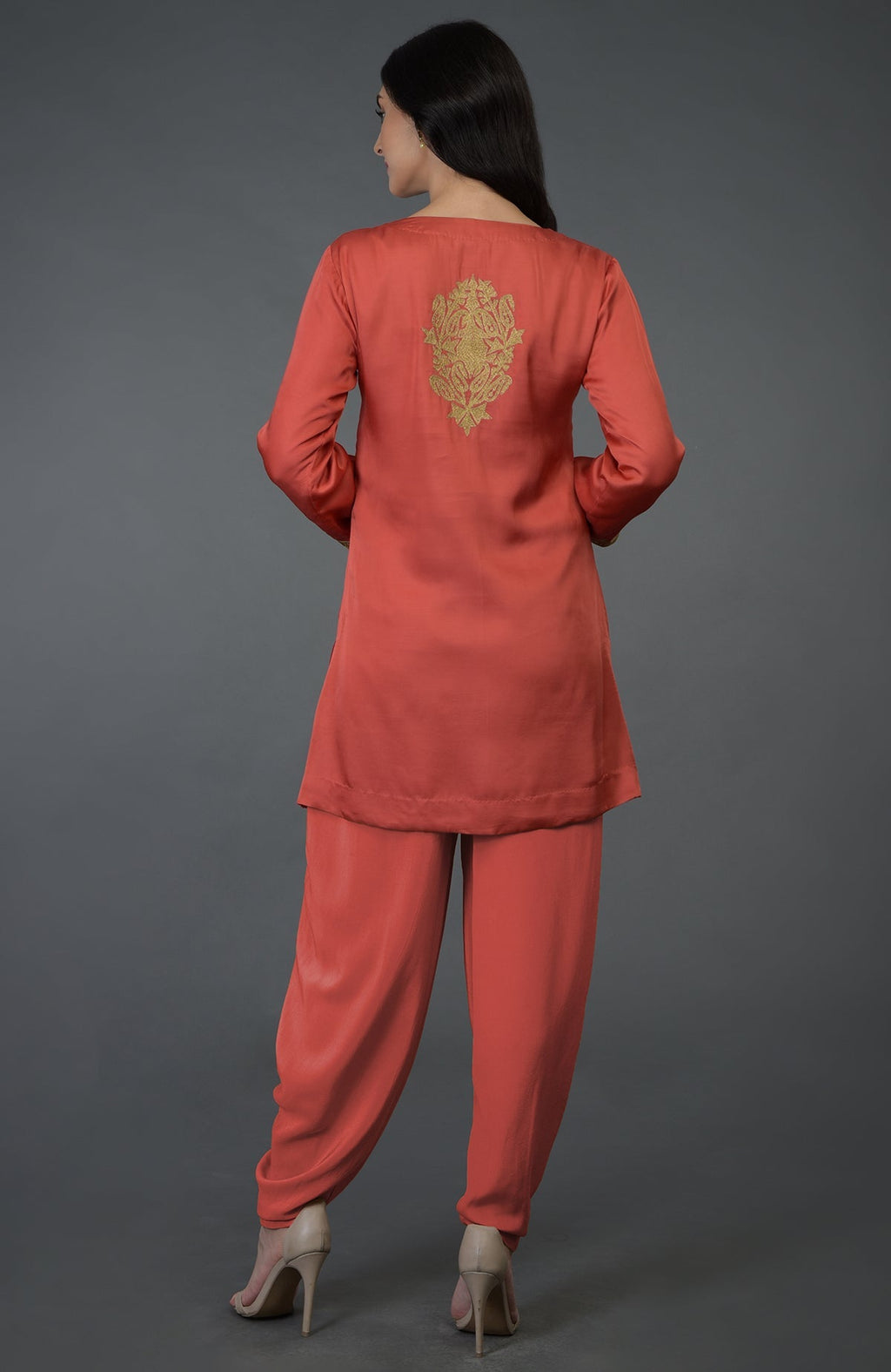 A woman models a living coral dhoti pants suit with gold Kashmiri tilla embroidery.