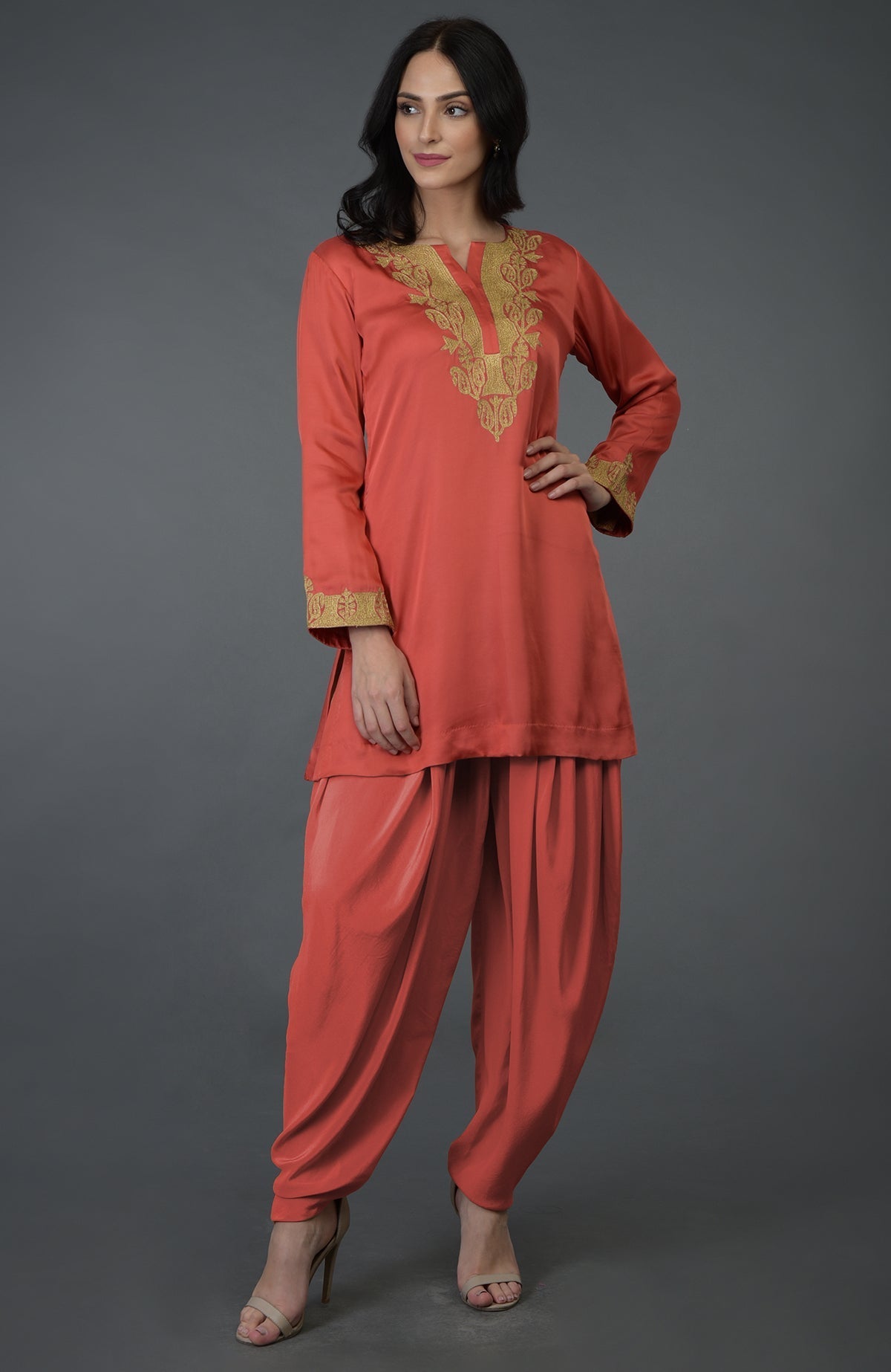 A woman models a living coral Kashmiri tilla embroidered dhoti pants suit.