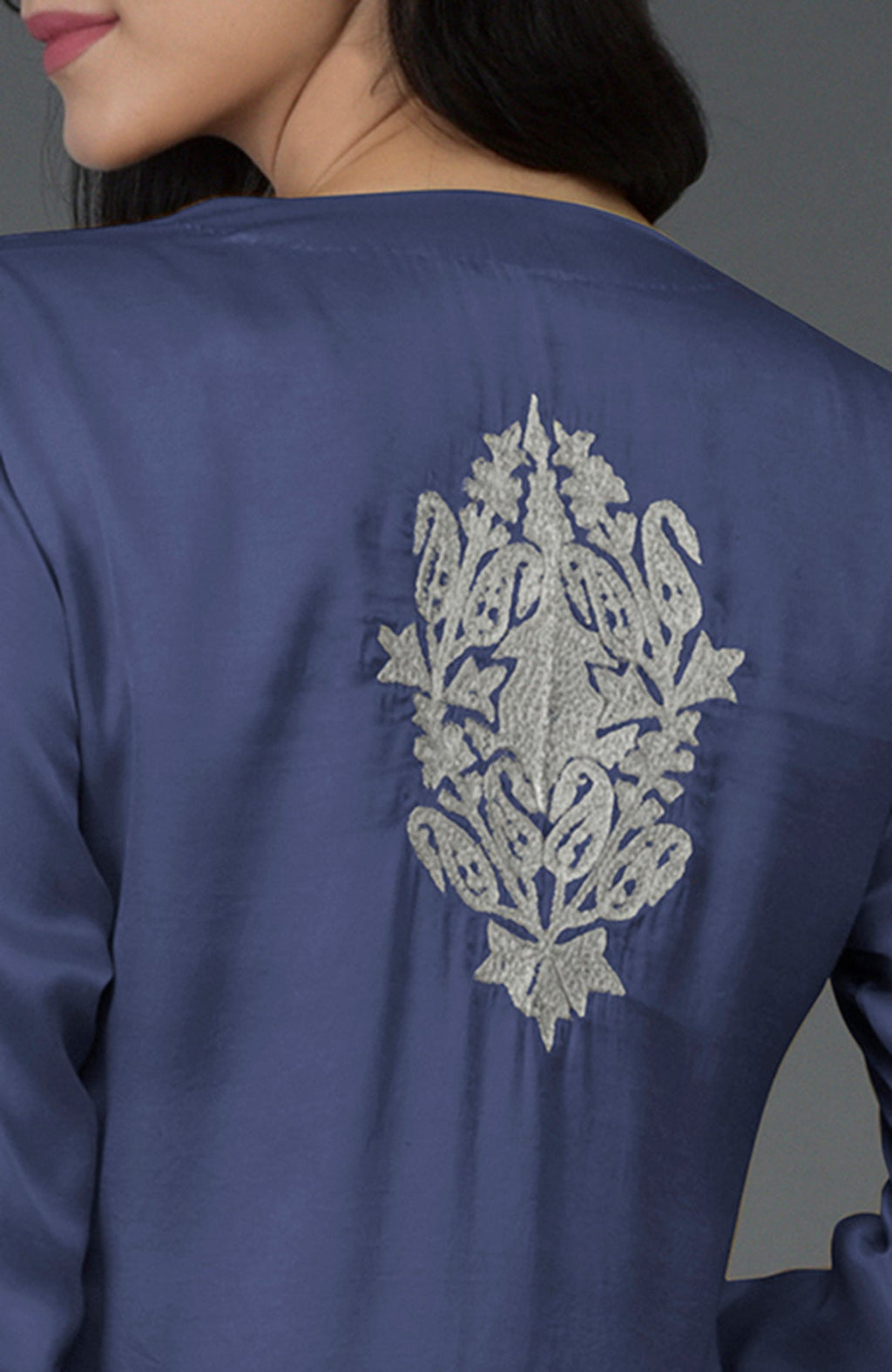 A woman models an iris blue kurta with silver Kashmiri tilla embroidery on the back.