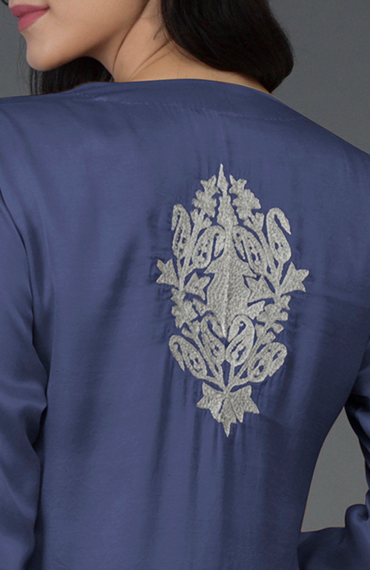 A woman models an iris blue kurta with silver Kashmiri tilla embroidery on the back.