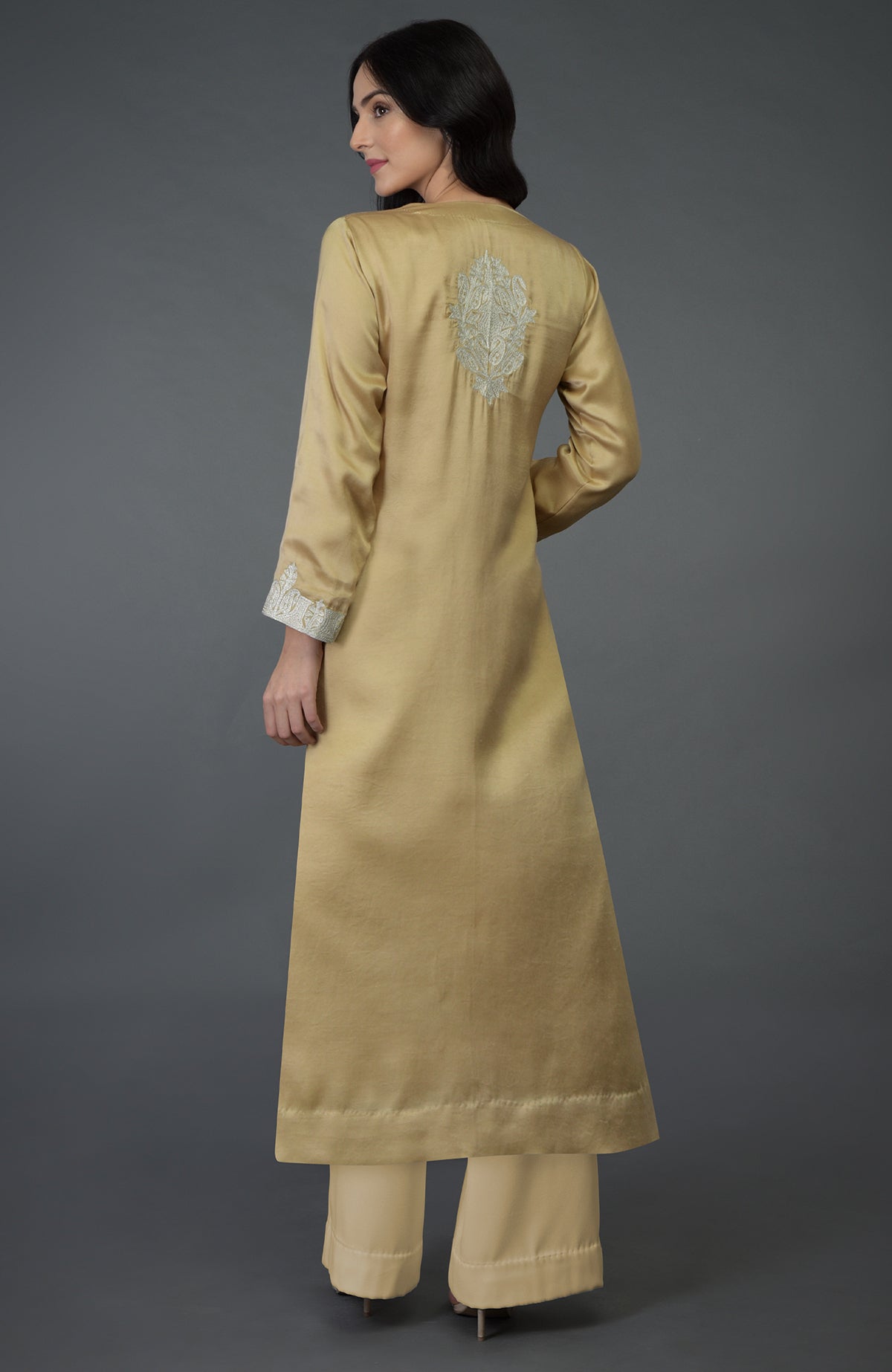 A woman models a beige gold Kashmiri tilla embroidered kurta set with wide-leg pants.