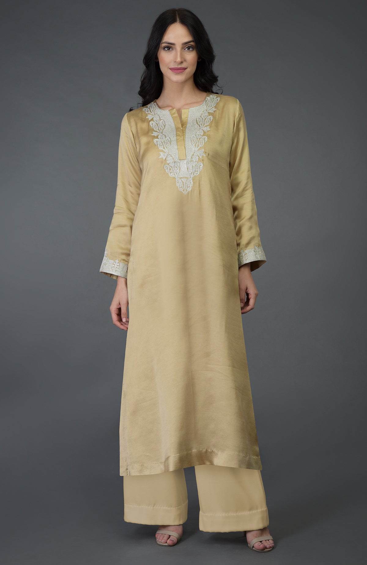 A woman models a beige gold Kashmiri tilla embroidered kurta set.