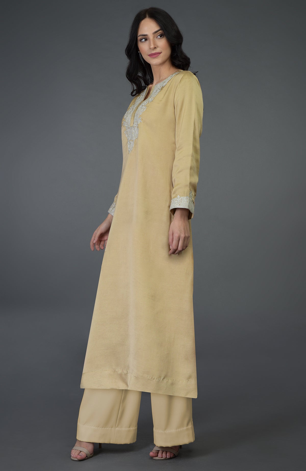A woman models a beige gold Kashmiri tilla embroidered kurta set.