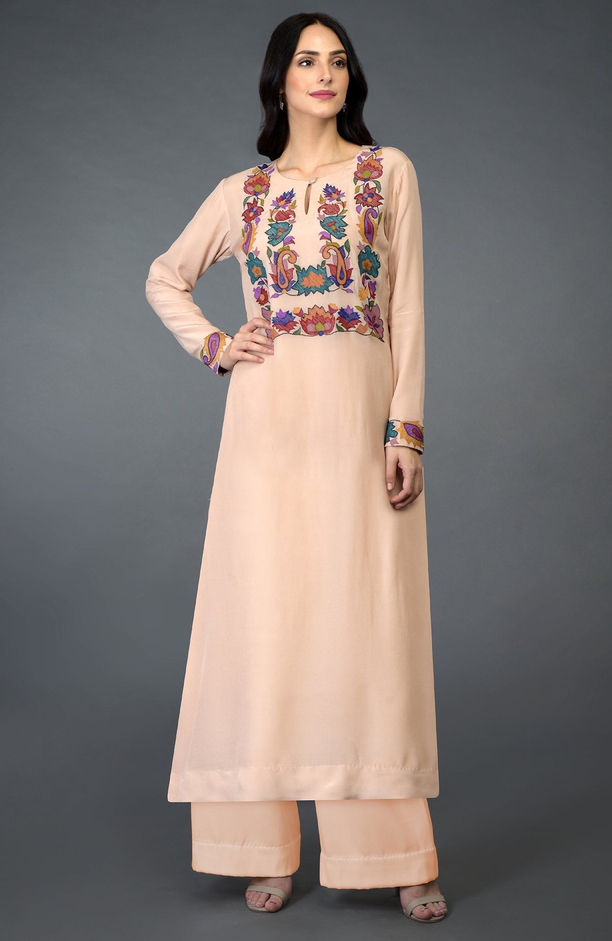 A woman models a tea rose kani art embroidered kurta set with colorful floral patterns.