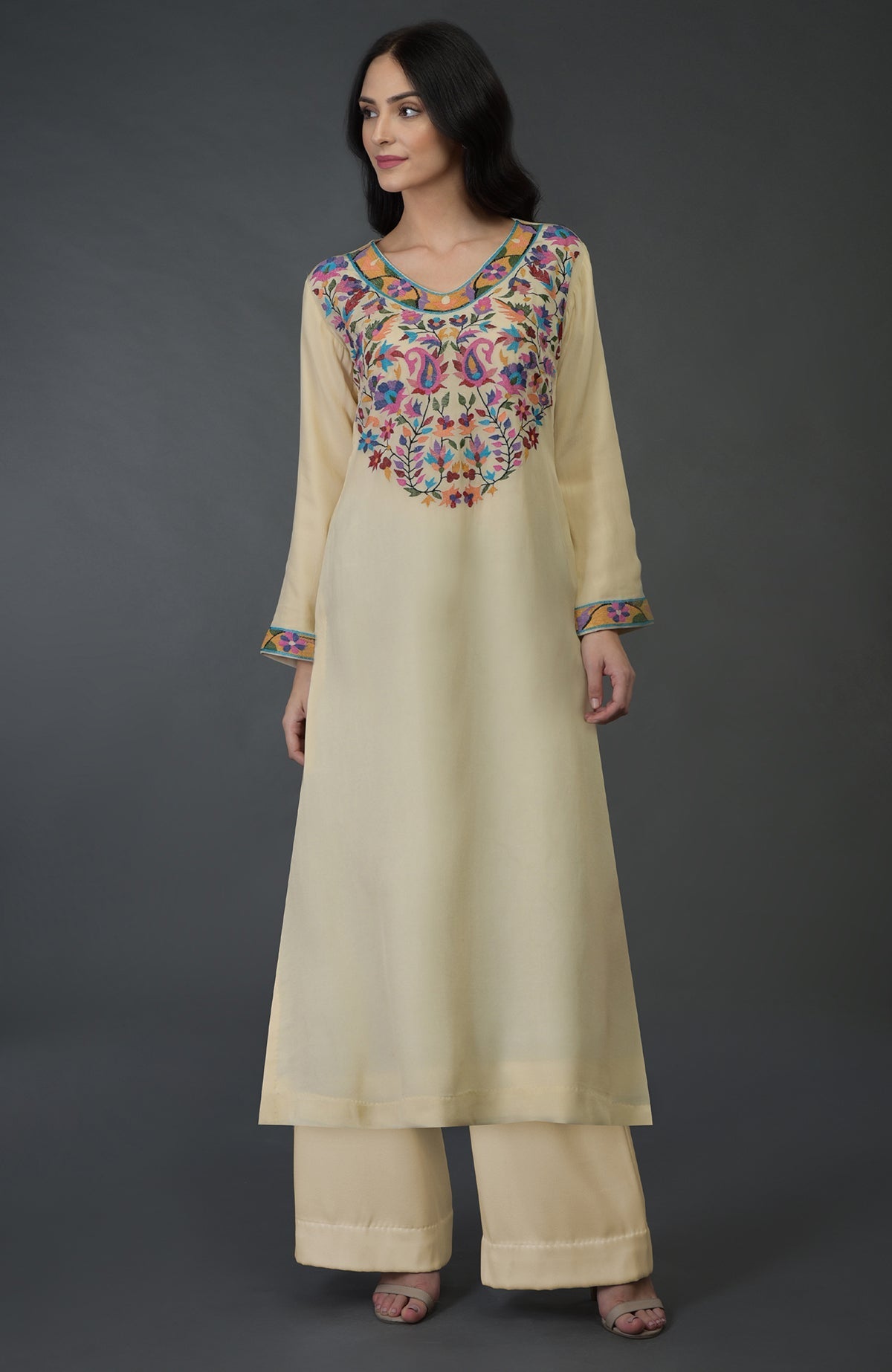 A woman models a deep cream kurta set with colorful Kani art embroidery.
