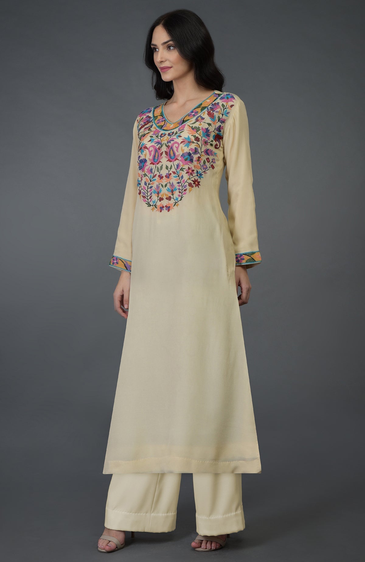 A woman models a deep cream kurta set with colorful Kani art embroidery.
