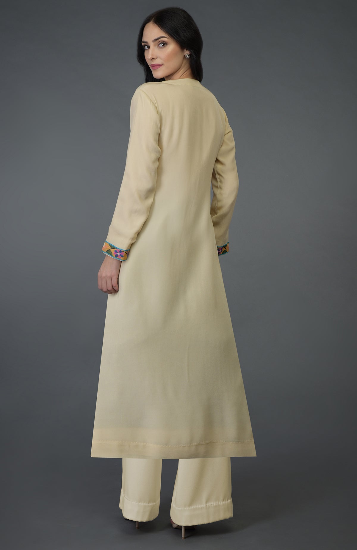 A woman models a deep cream kurta set with colorful Kani art embroidery on the sleeves.