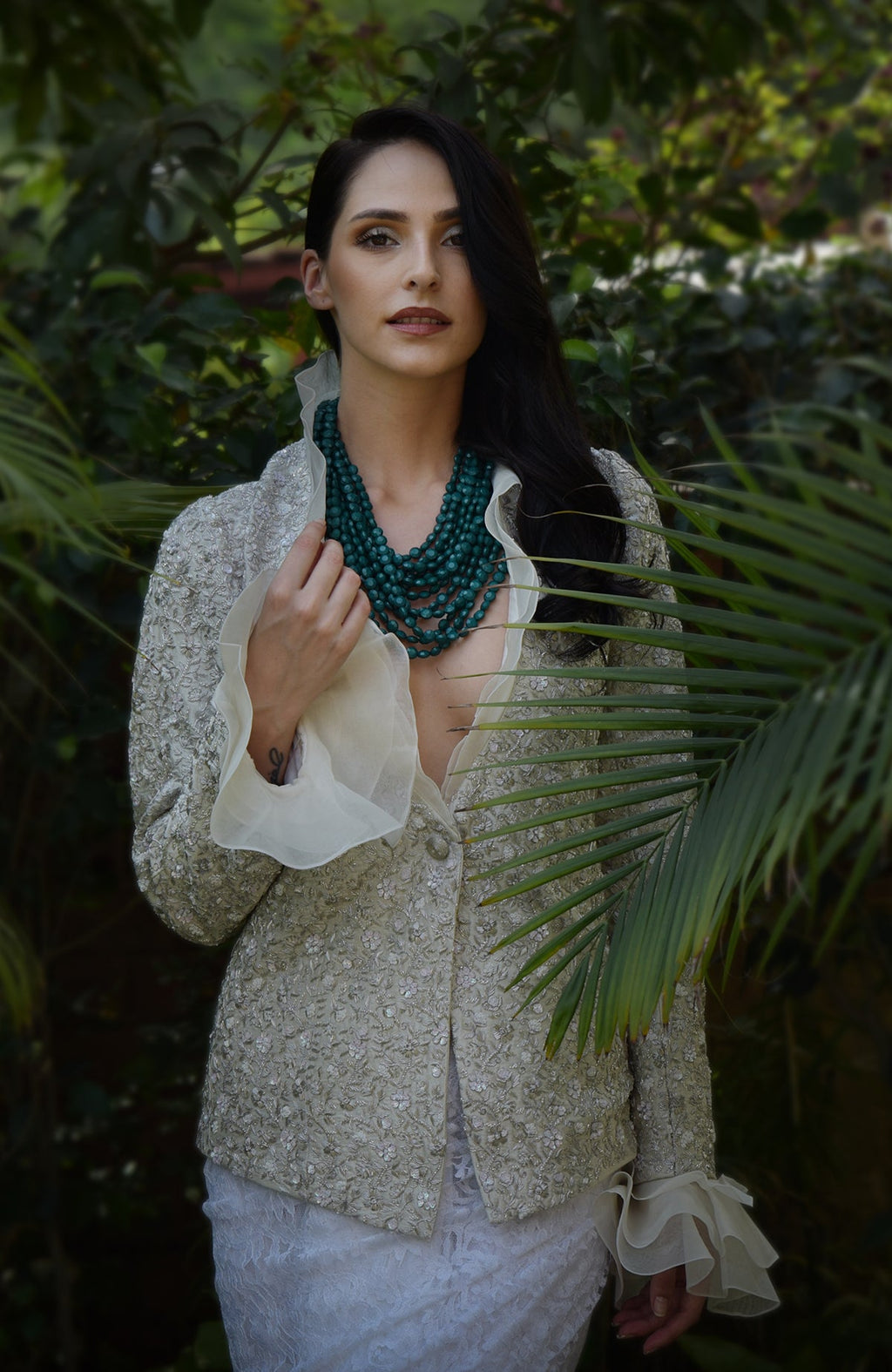 Woman wears a white sequin and bead embroidered jacket with a green beaded necklace.