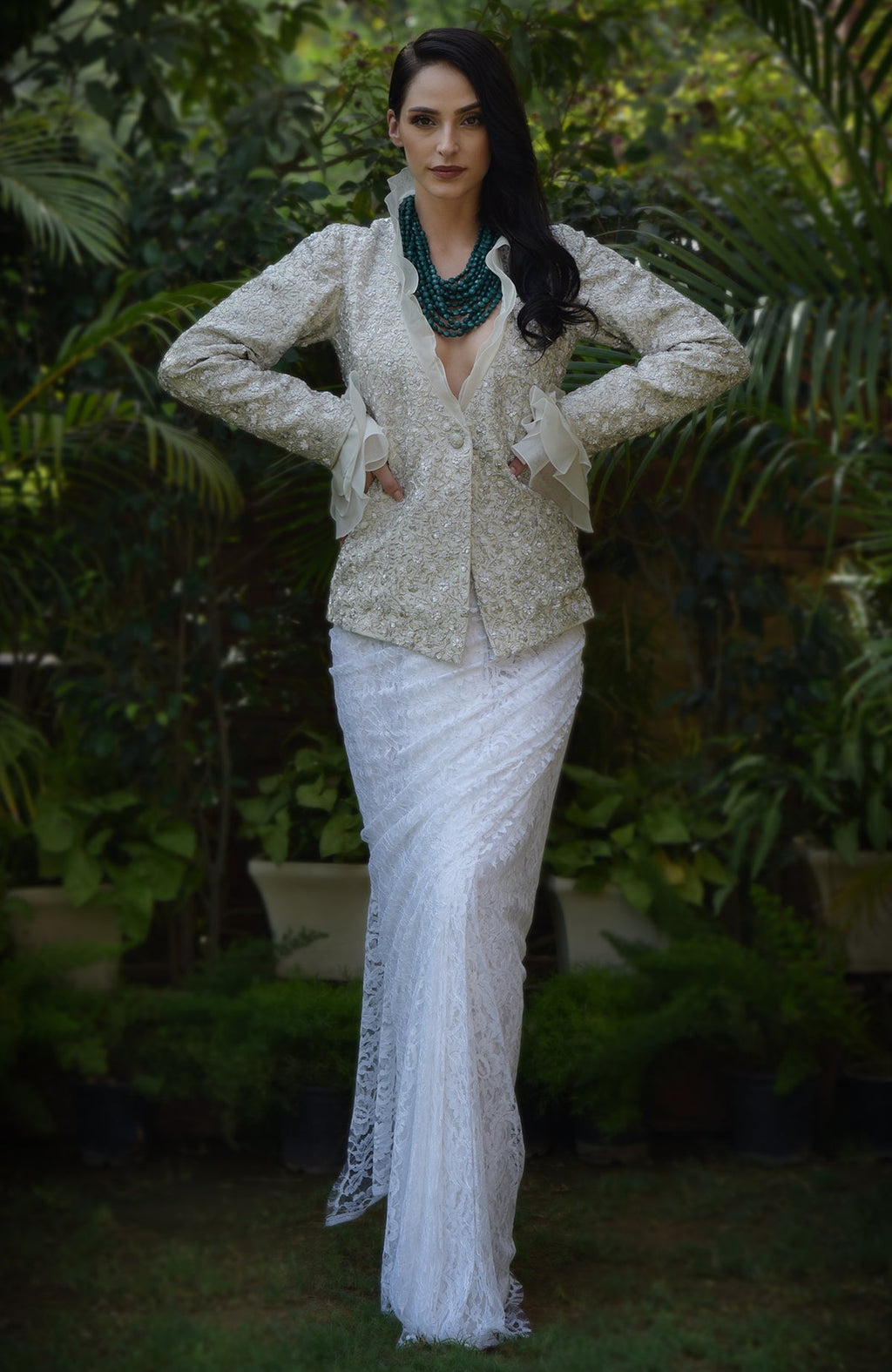 A woman models a white sequin and bead embroidered jacket with a white lace skirt.