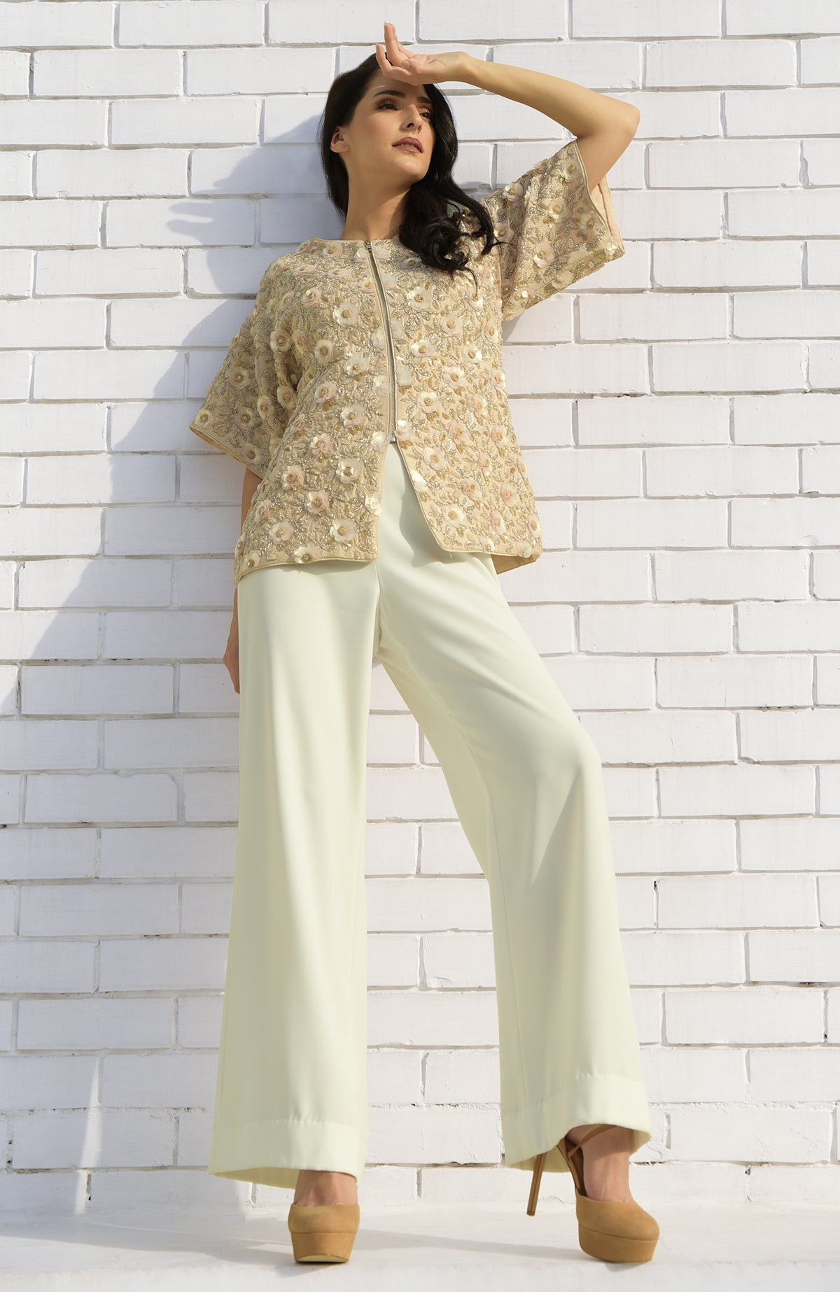 A woman models a light peach sequin and beaded hand-embroidered jacket with wide-leg pants.
