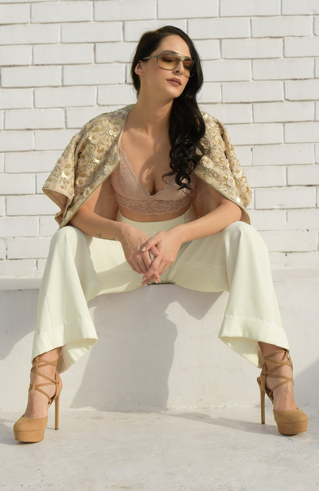 Woman in a sequin and beaded jacket, light peach bralette, and cream pants.