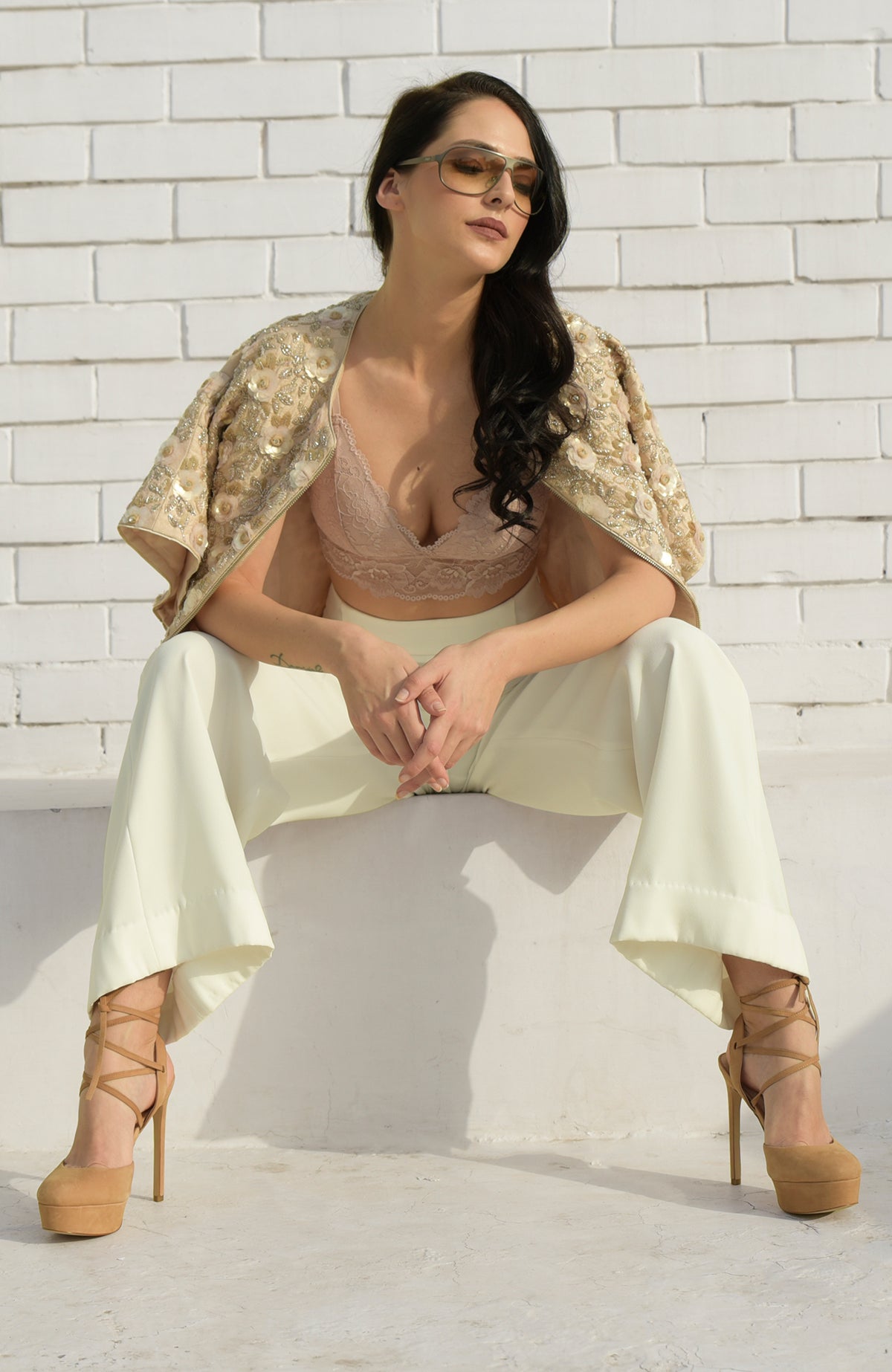 Woman in a sequin and beaded jacket, light peach bralette, and cream pants.
