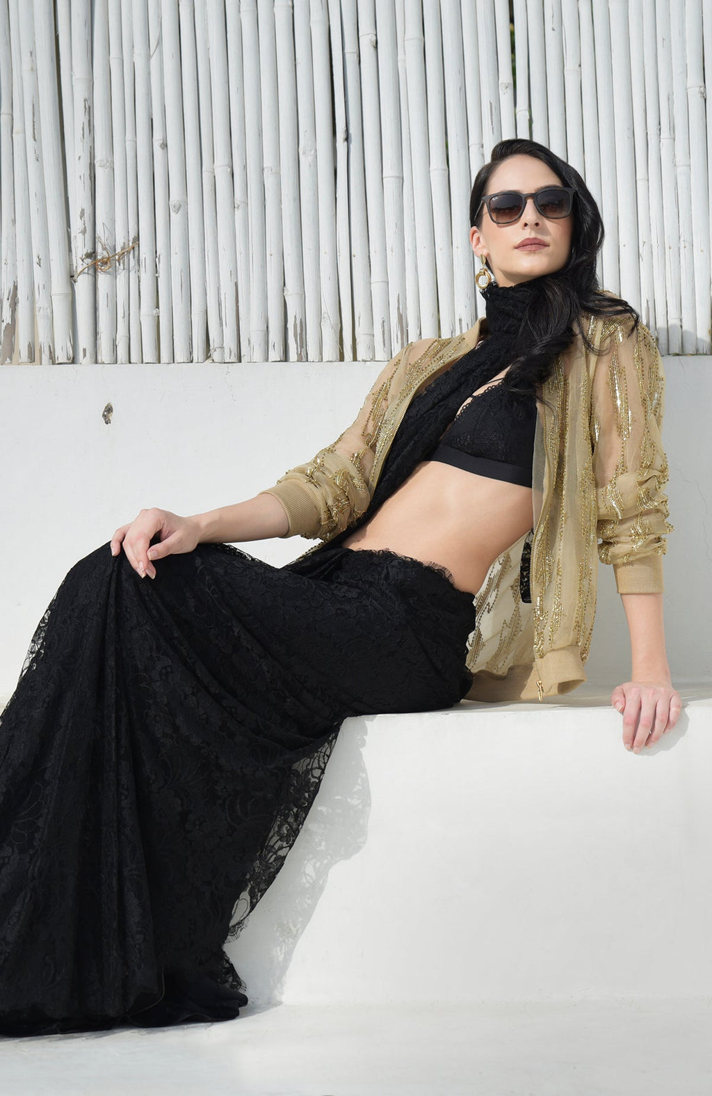 A woman models a gold sequin and bead embroidered bomber jacket over a black lace outfit.