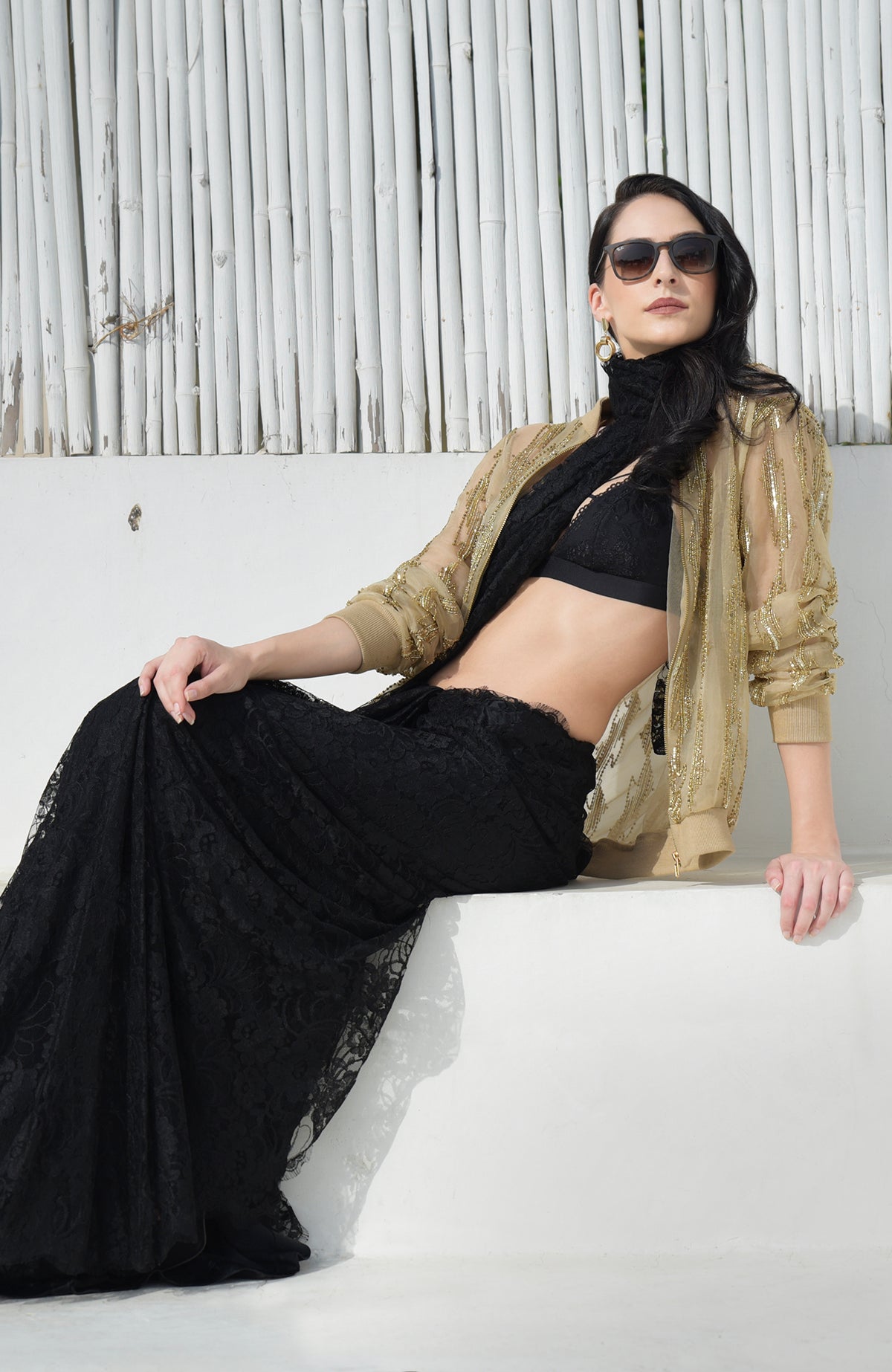 A woman models a gold sequin and bead embroidered bomber jacket over a black lace outfit.