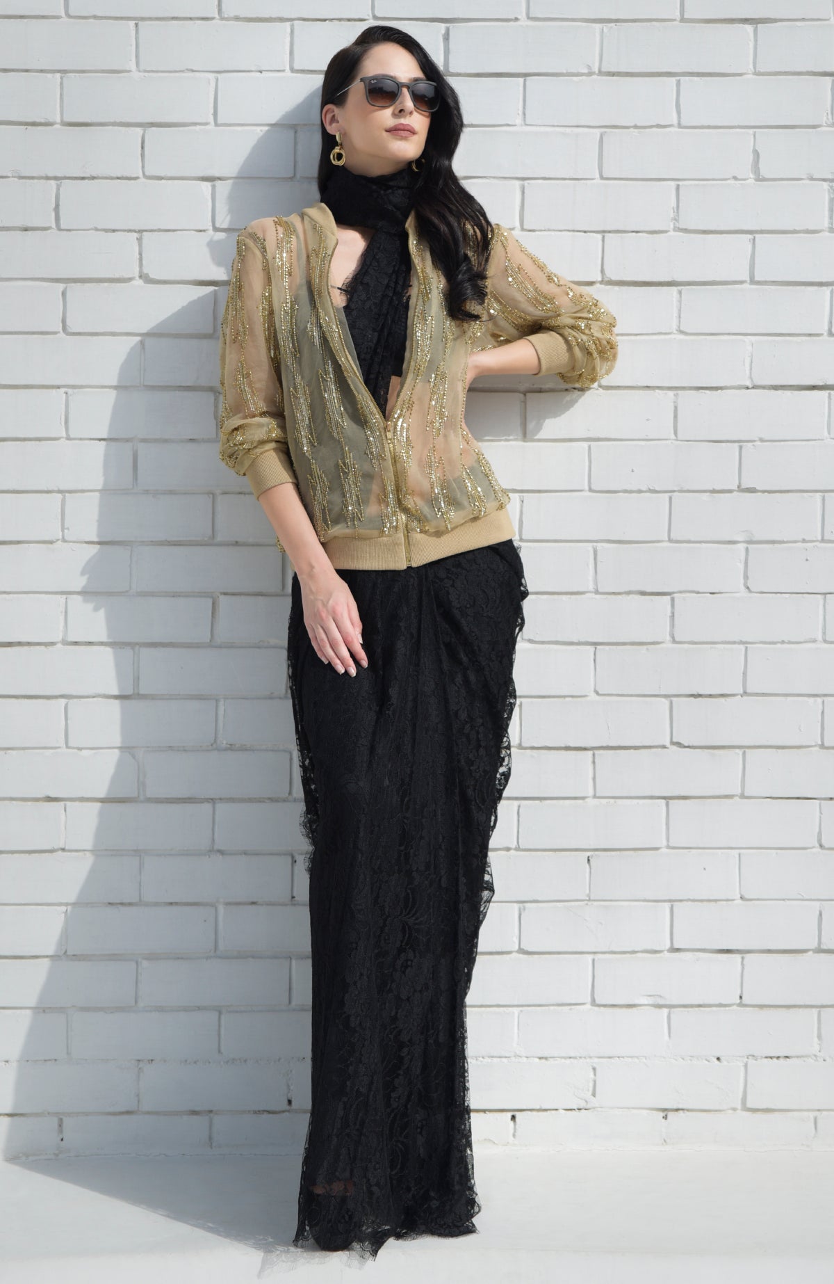 A woman models a gold sequin and bead embroidered bomber jacket over a black lace dress.