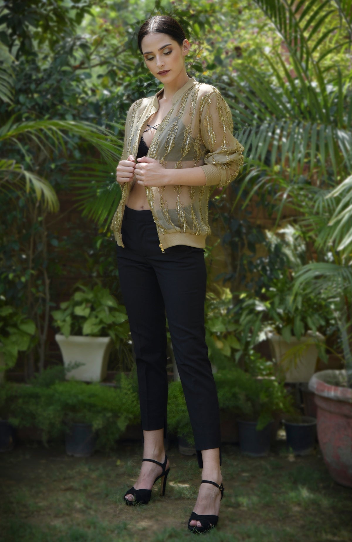 A woman models a gold sequin and bead embroidered bomber jacket over a black bra and pants.