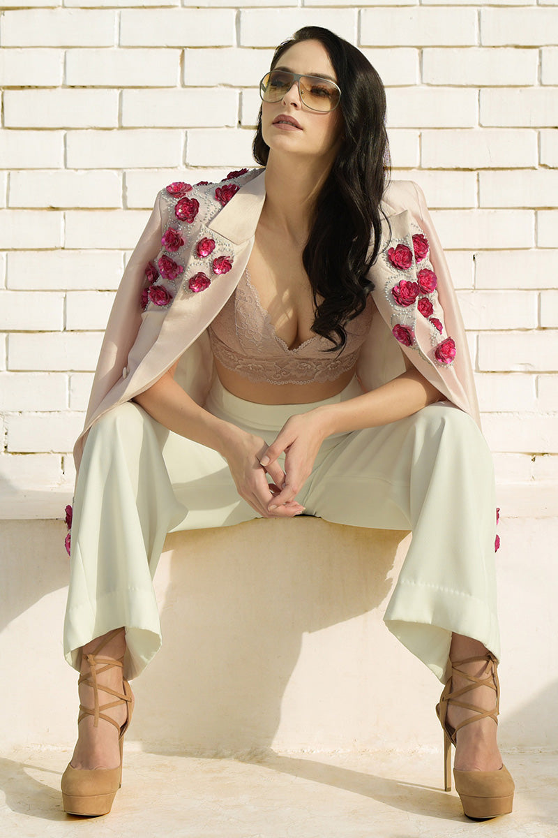 A woman models a pale pink hand-embroidered jacket with red floral embellishments.