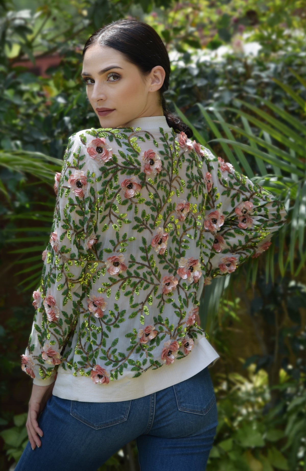 A woman models a cream silk chiffon bomber jacket with 3D coral florals and beaded leaves.
