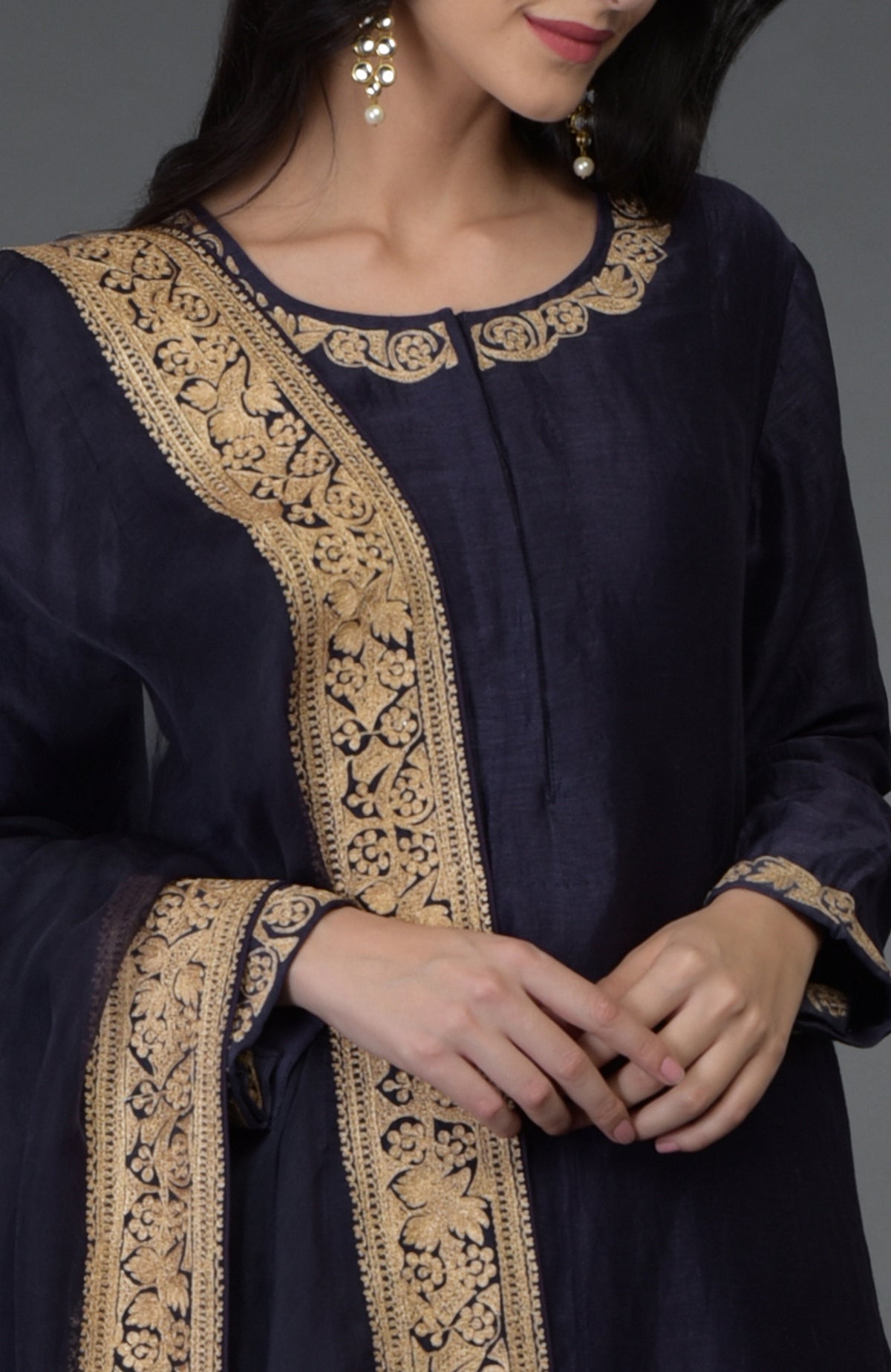 Woman in an eclipse blue suit with gold tilla embroidery on the neckline, sleeves, and dupatta.