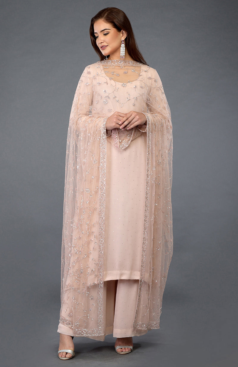 A woman models a nude pink handcrafted mukaish farshi palazzo suit with a sheer dupatta.