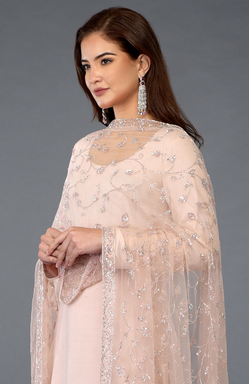A woman models a nude pink handcrafted mukaish farshi palazzo suit with an embroidered dupatta.