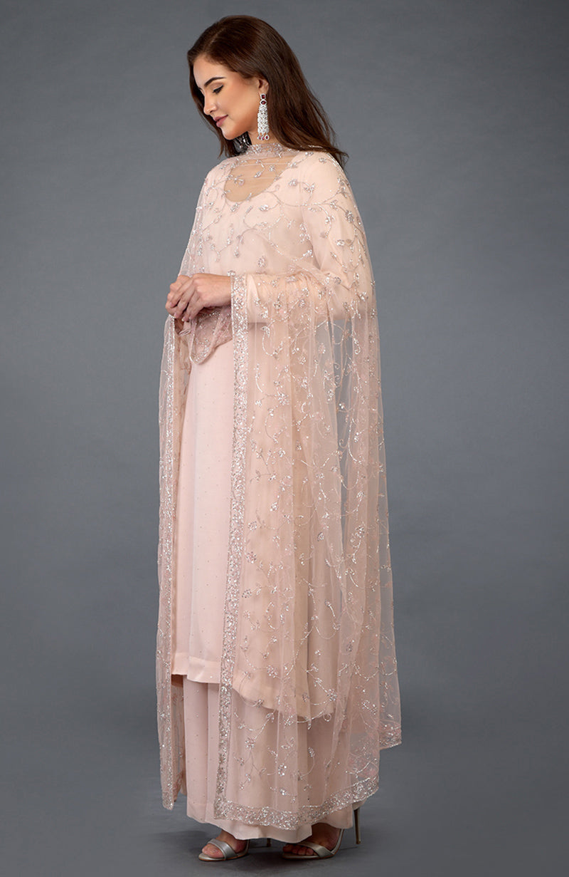 A woman models a nude pink handcrafted mukaish farshi palazzo suit with a sheer dupatta.