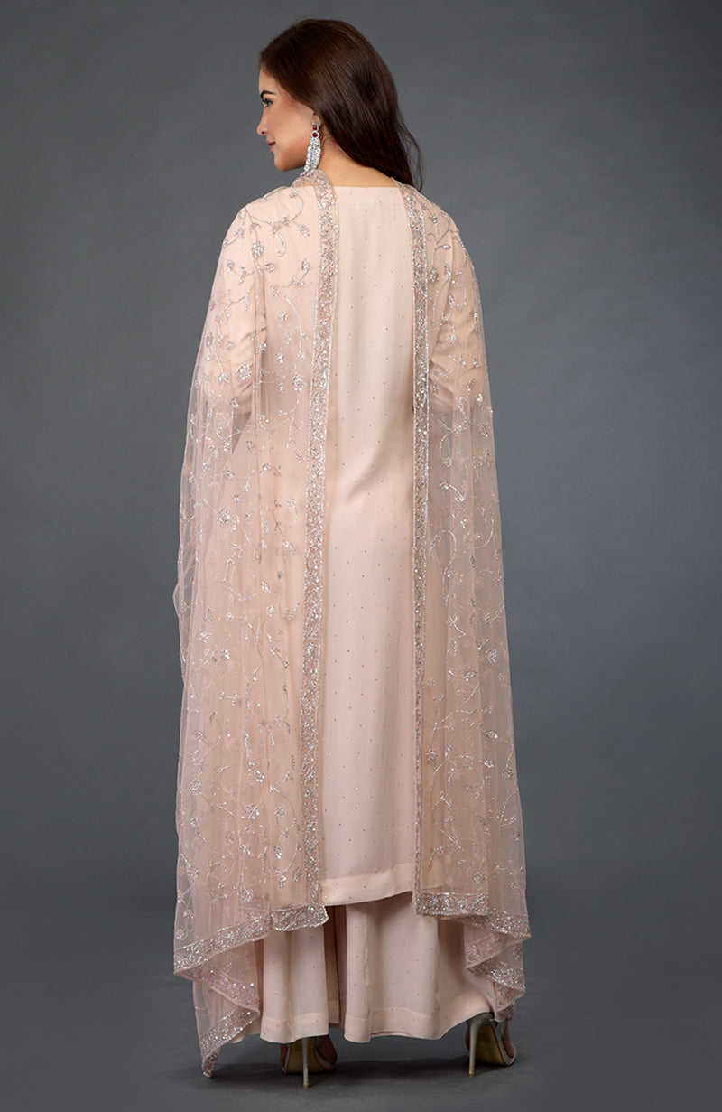 A woman from behind wears a nude pink palazzo suit with a sheer, embellished overlay.