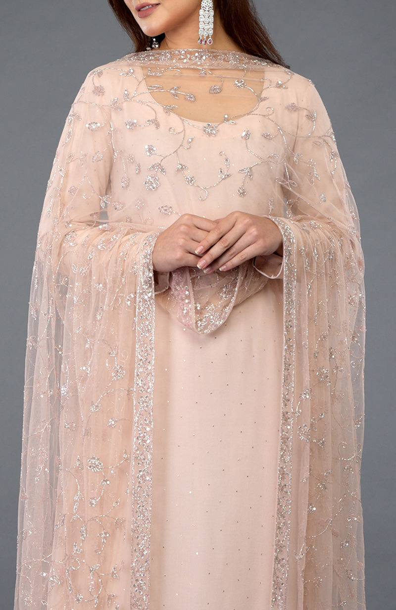 A woman models a nude pink handcrafted mukaish farshi palazzo suit with a sheer dupatta.