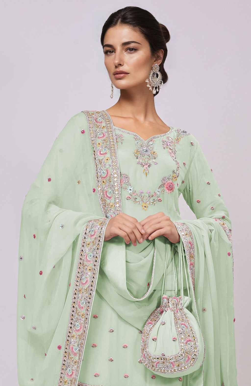 A woman models a sage green sharara set with intricate embroidery and a matching potli bag.