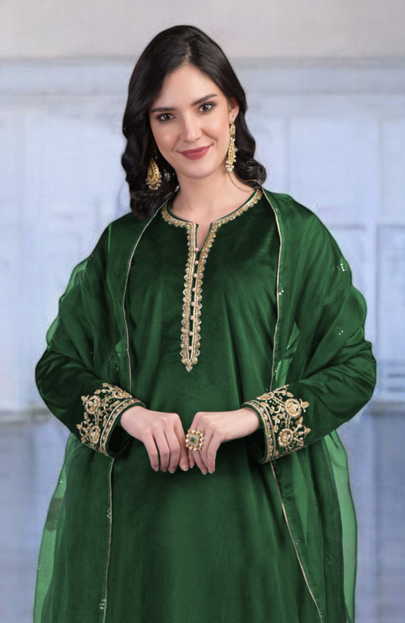 An elegant woman in an emerald green velvet kurta set with gold embroidery.