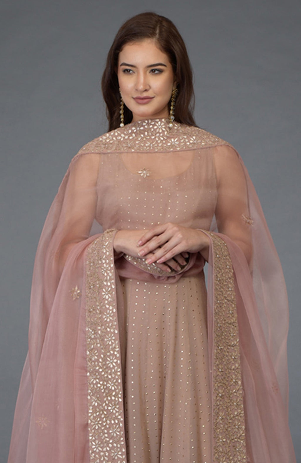 A woman models a dusky pink Anarkali suit with a matching embroidered dupatta.