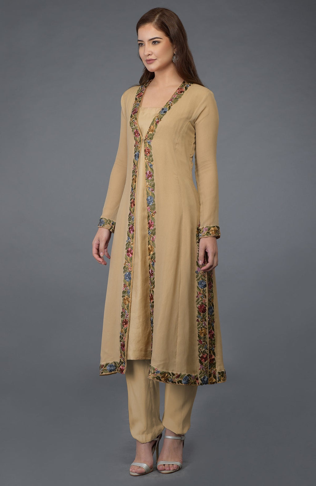 A woman models a beige Parsi Gara embroidered overlay suit with silver heels.