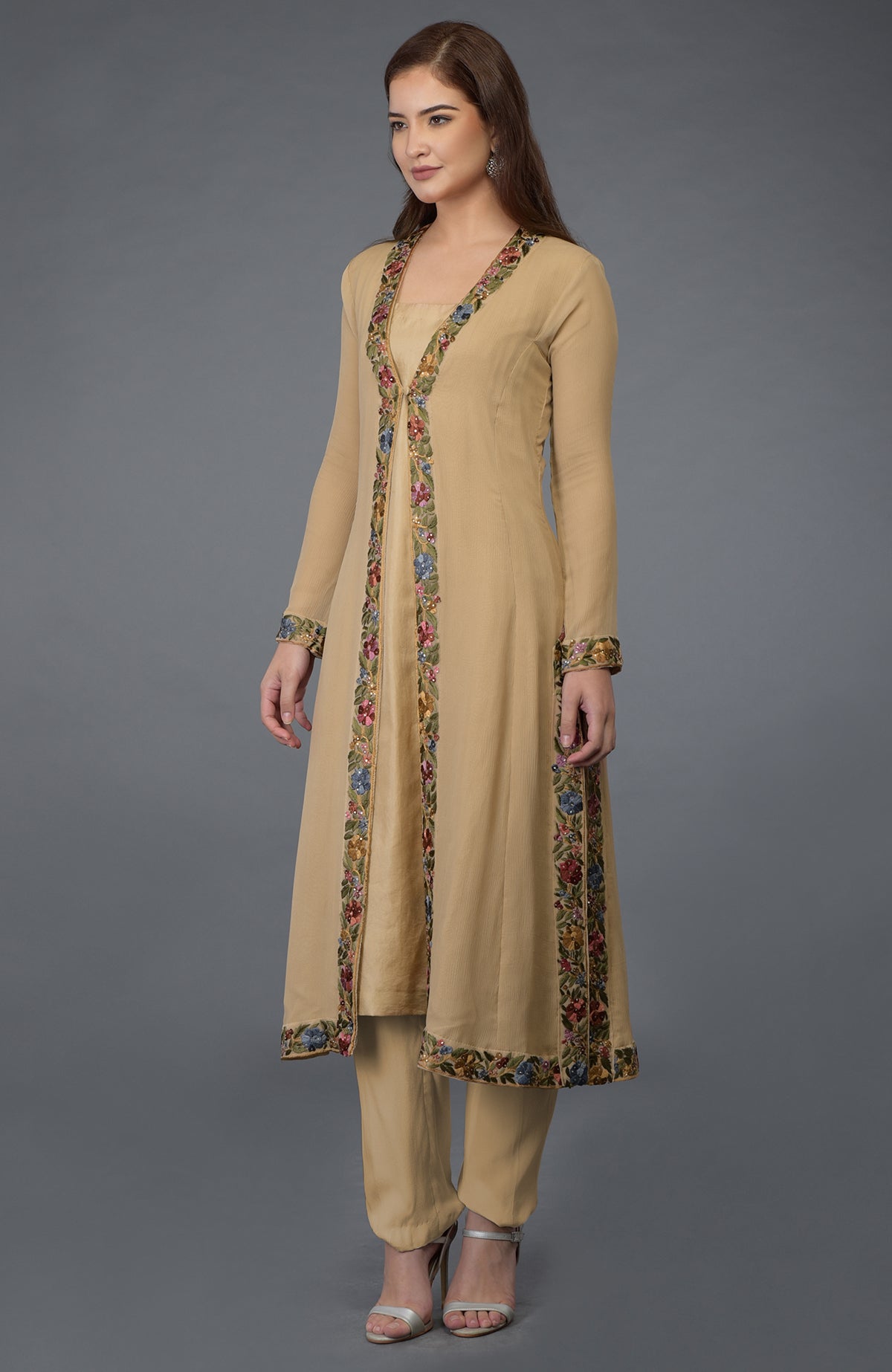 A woman models a beige Parsi Gara embroidered overlay suit with silver heels.