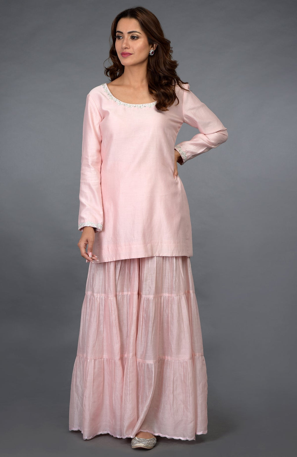 A woman models a pink gharara suit with silver embroidery and sequin details.