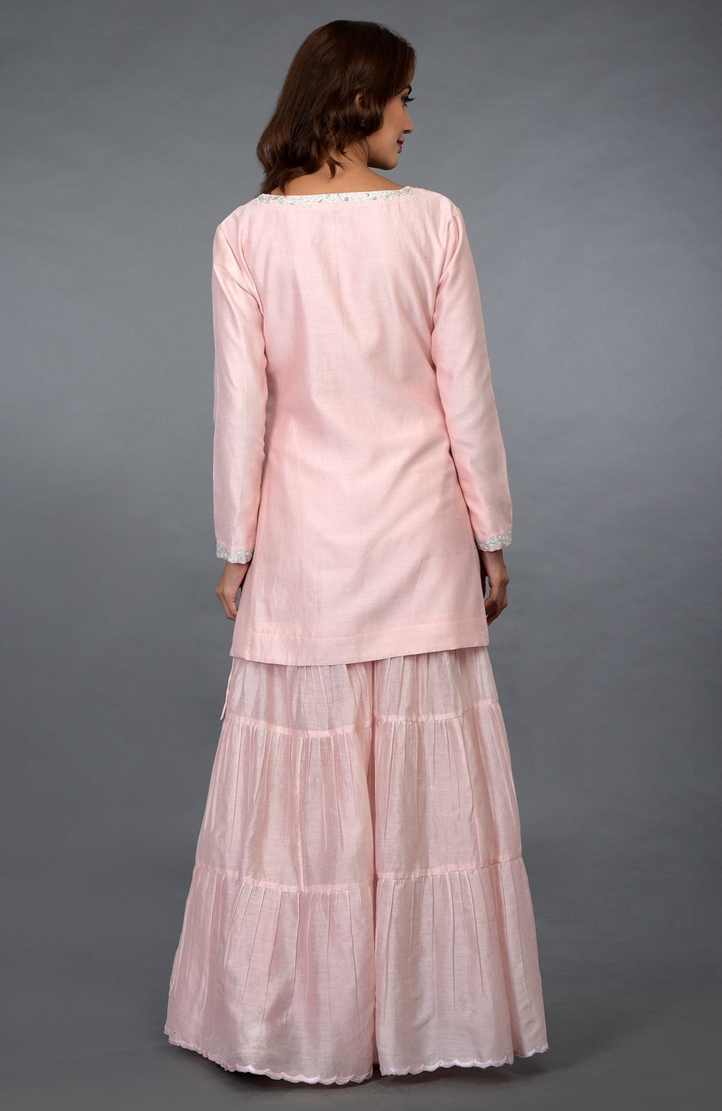 A woman models a pink gharara suit with silver embroidery.