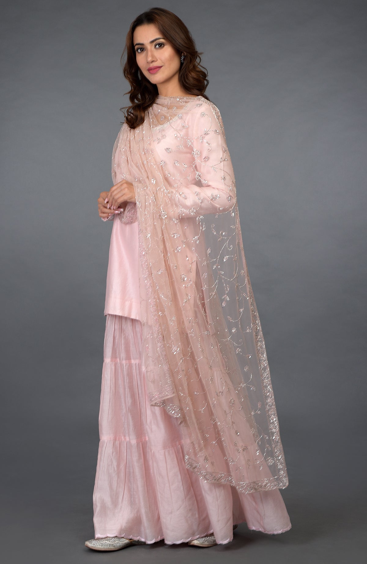 A woman models a pink-silver zari, beads, and sequin embroidered gharara suit.