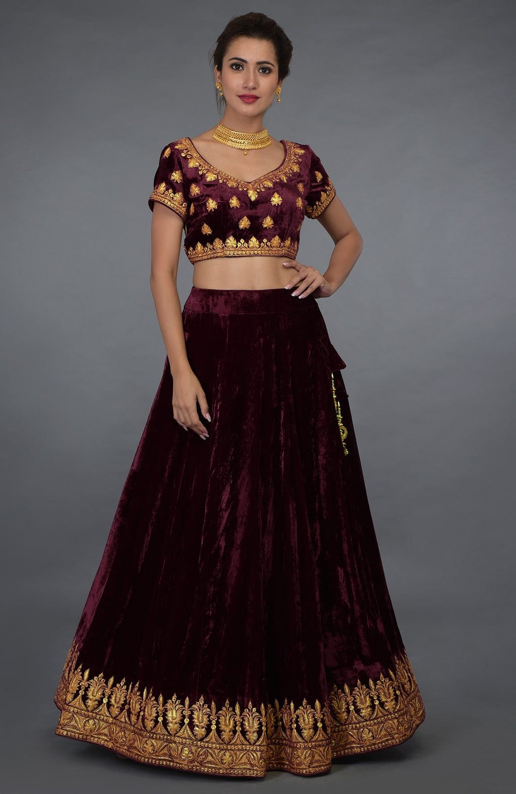 A woman models a burgundy velvet lehenga with gold tilla embroidery.