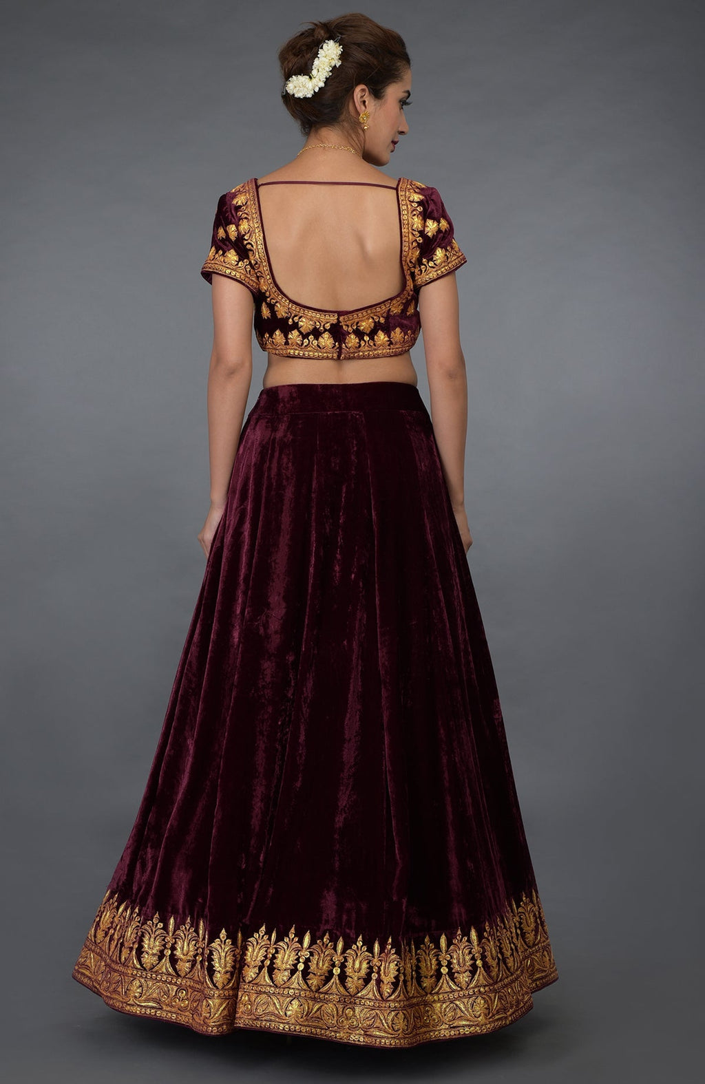 A woman models a burgundy velvet lehenga with gold tilla embroidery.