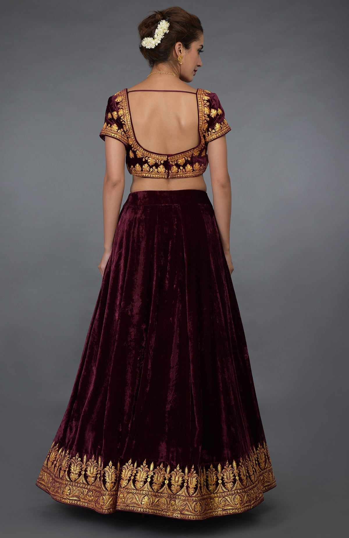 A woman models a burgundy velvet lehenga with gold tilla embroidery.