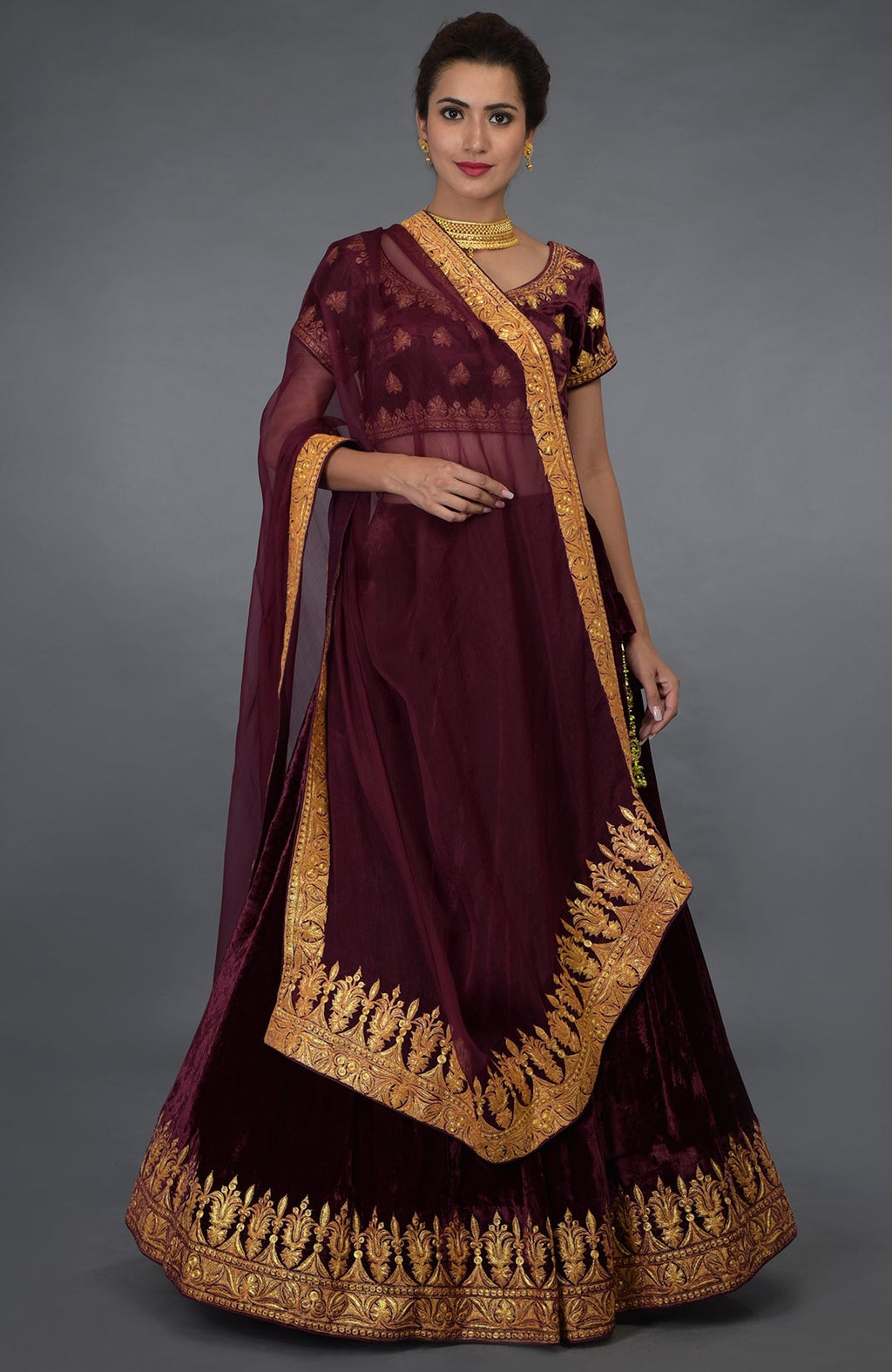 A woman models a burgundy Kashmiri Tilla embroidered lehenga outfit.