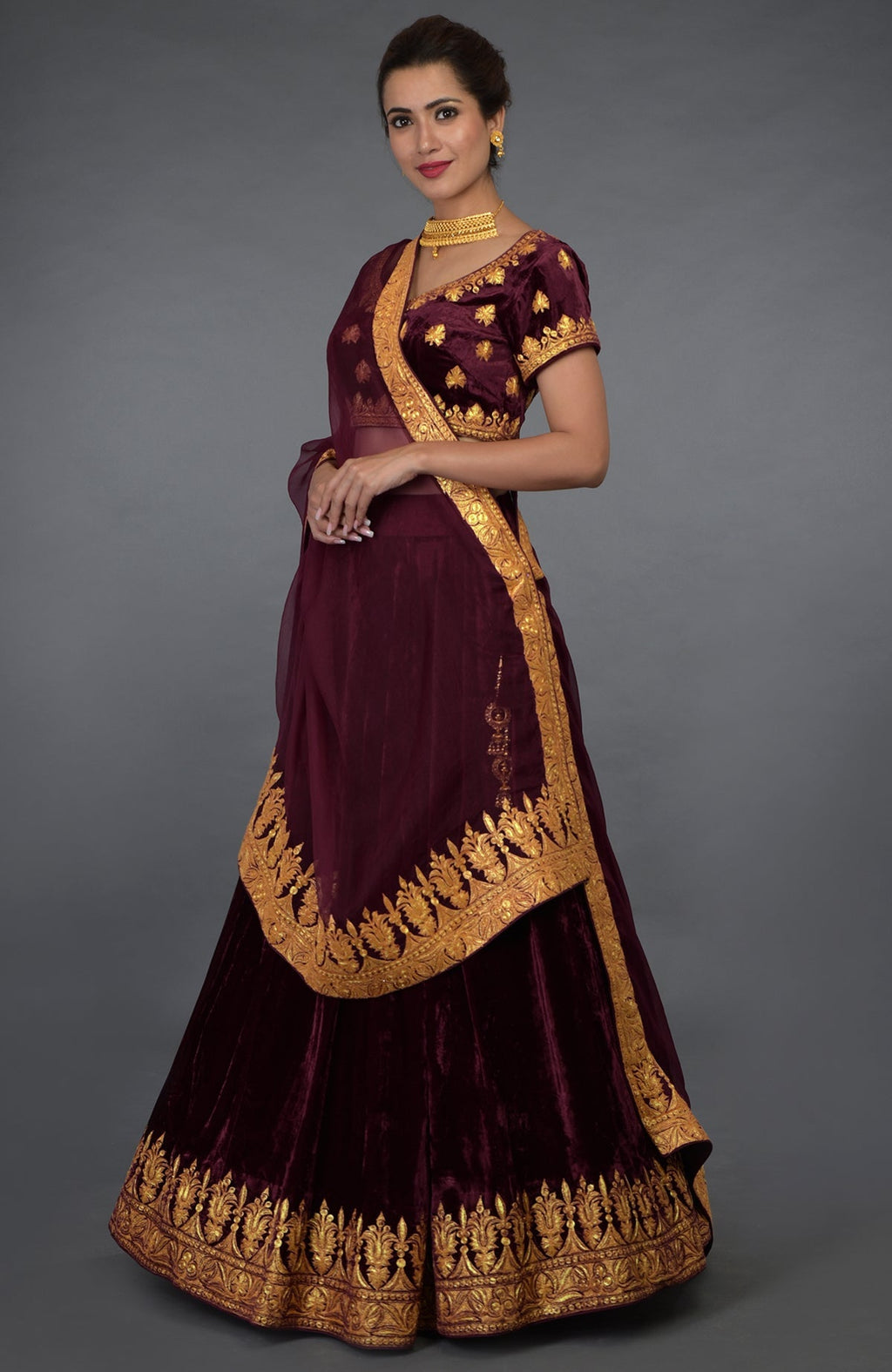 A woman models a burgundy lehenga with gold tilla embroidery and a matching dupatta.