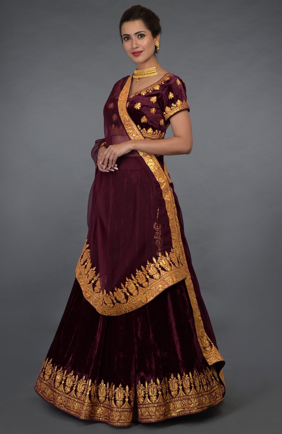 A woman models a burgundy lehenga with gold tilla embroidery and a matching dupatta.