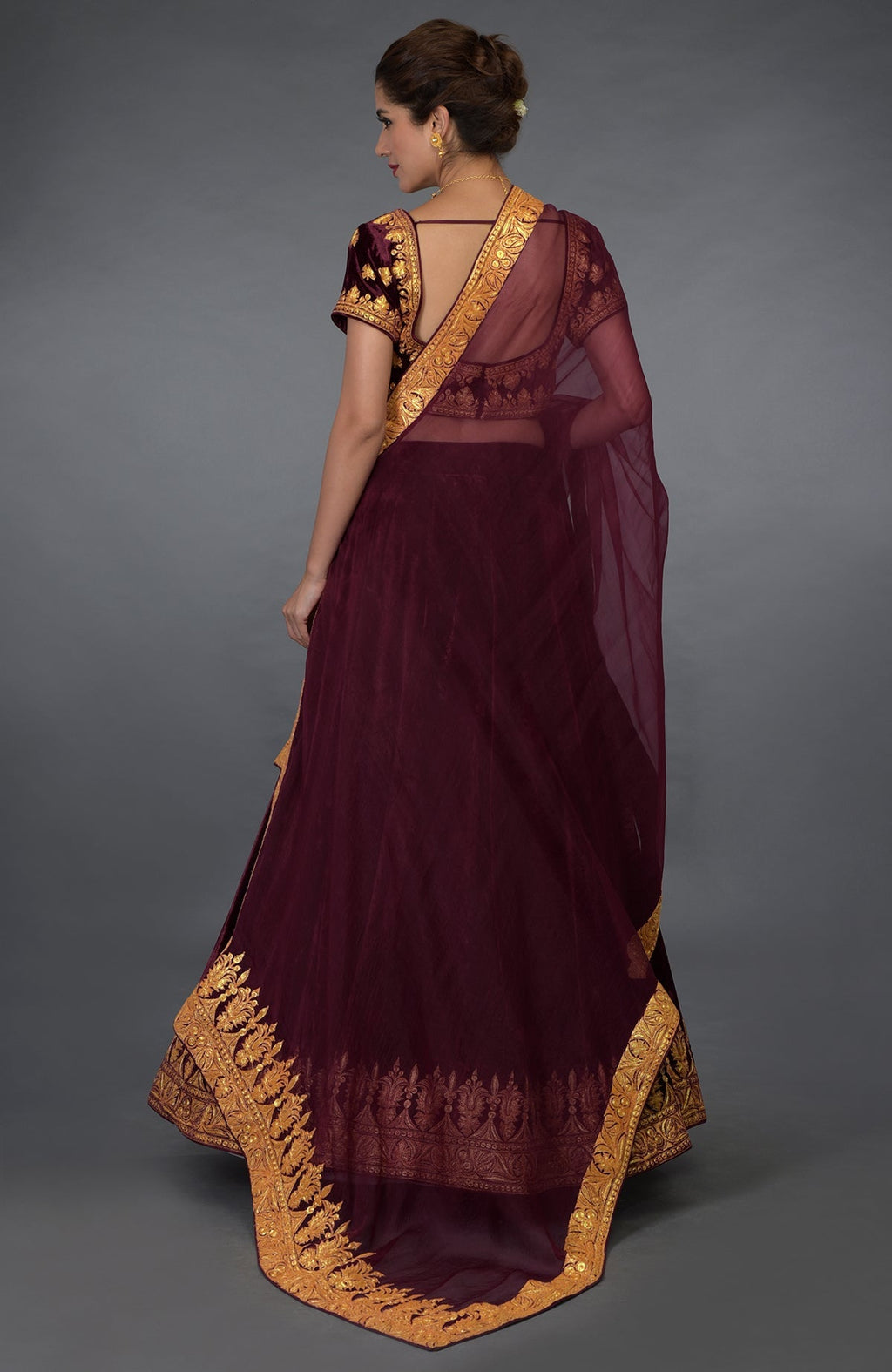 A woman models a burgundy lehenga with gold tilla embroidery.